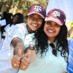 Two South Asian female college students smiling an giving a thumbs up to the camera.