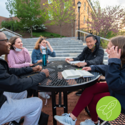 A group of students sitting outside around a table smiling.