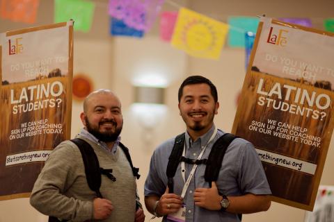 Two latino males with backpacks smiling at camera with a background of papel picado