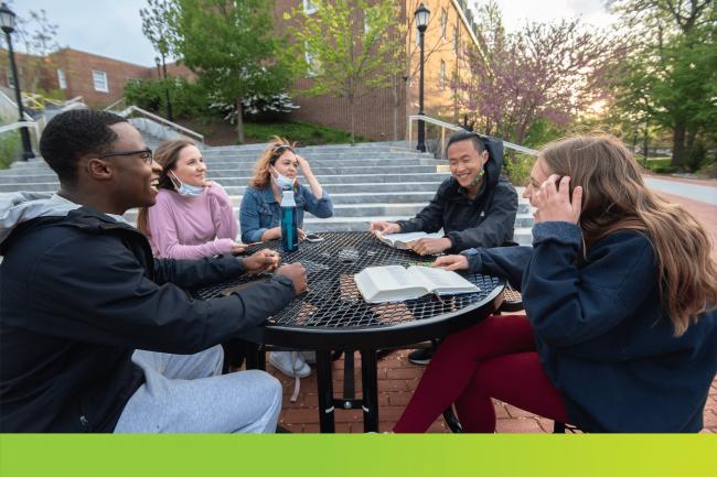 A group of students sitting outside around a table smiling.