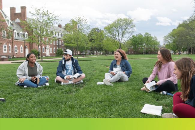 A group of students sitting in a circle on a campus lawn. 